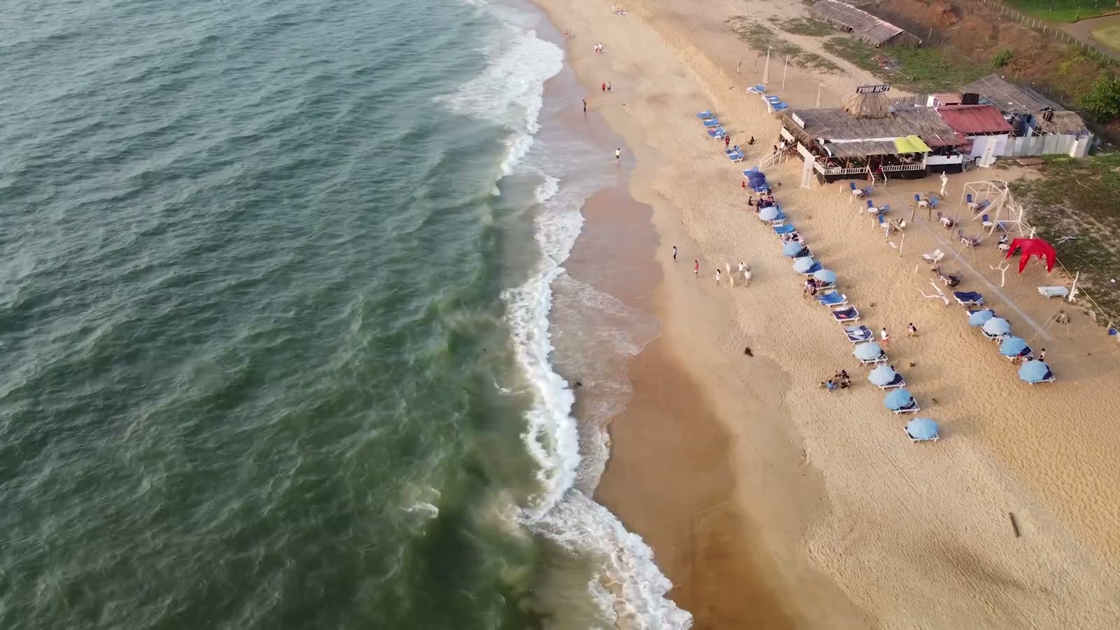 Waves wash along the sandy Goa coastline in an aerial view.