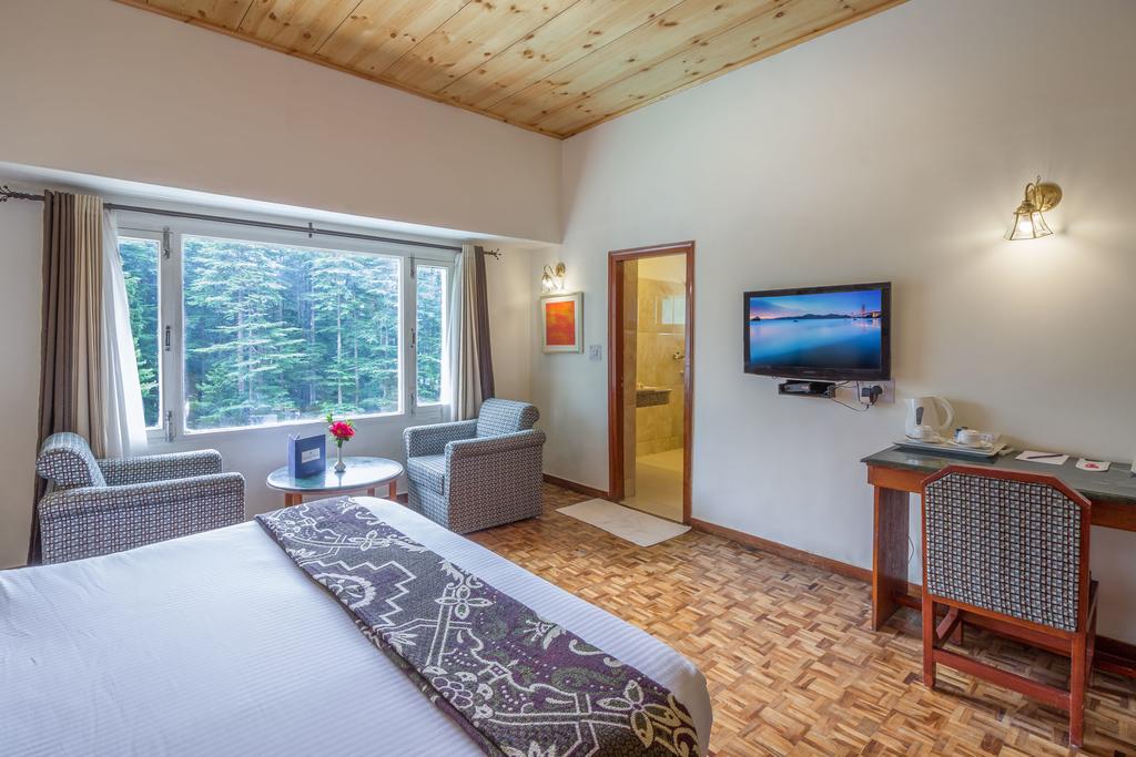 Guest room with a seating area and a large window overlooking trees, shown on the Golden Tulip Manali listing.