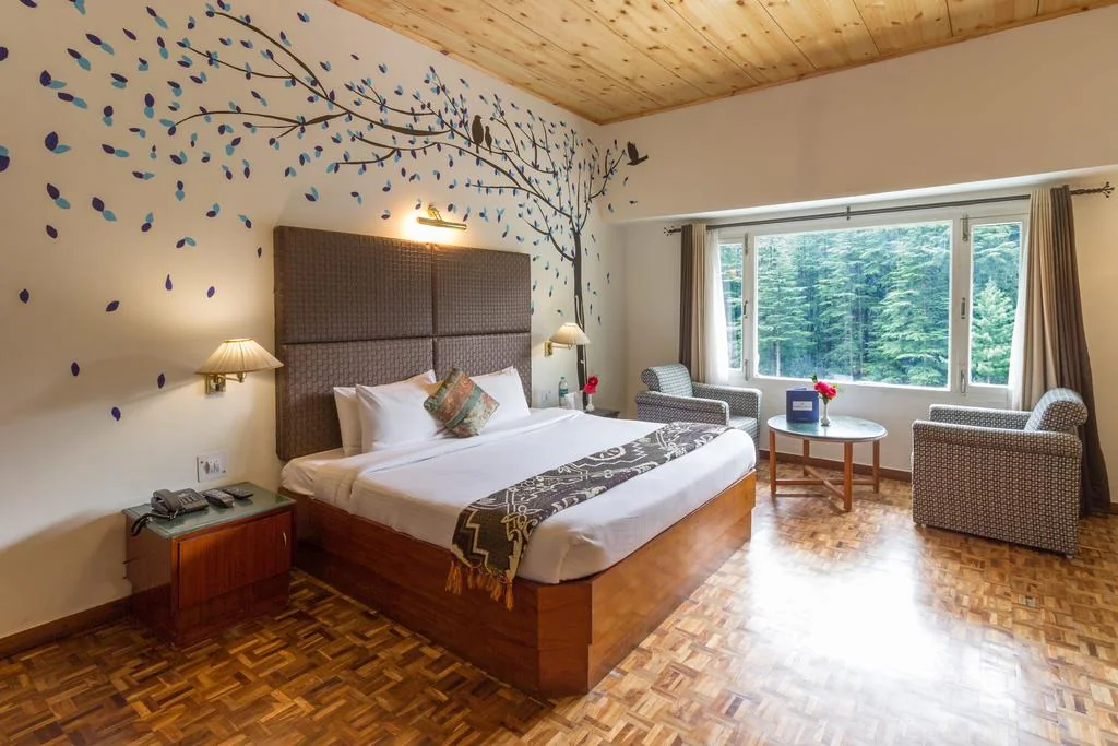 Double room with a tree-pattern wall, seating and large windows.