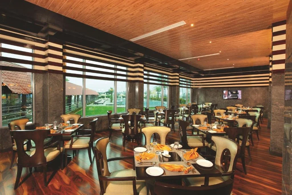 Restaurant tables set beneath a wood-toned ceiling beside broad windows.