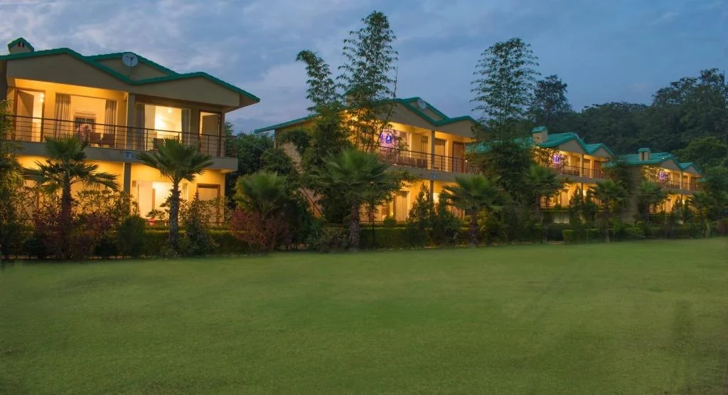 Illuminated resort buildings behind a broad garden lawn at dusk.
